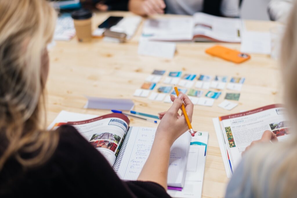 A diverse group of students in a language school classroom, engaging in interactive Spanish learning activities. The room is bright and colorful, with educational materials and Spanish cultural decorations.